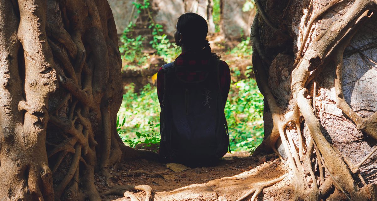 A perimenopausal woman rests in the forest in a tunnel of trees