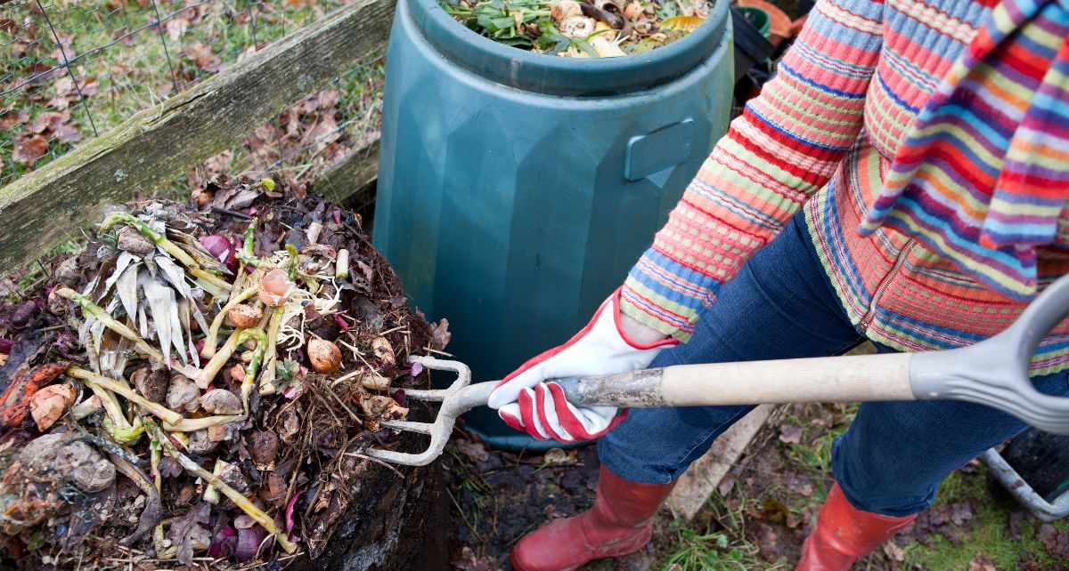 A person standing with a garden tool digging in a garden compost heap