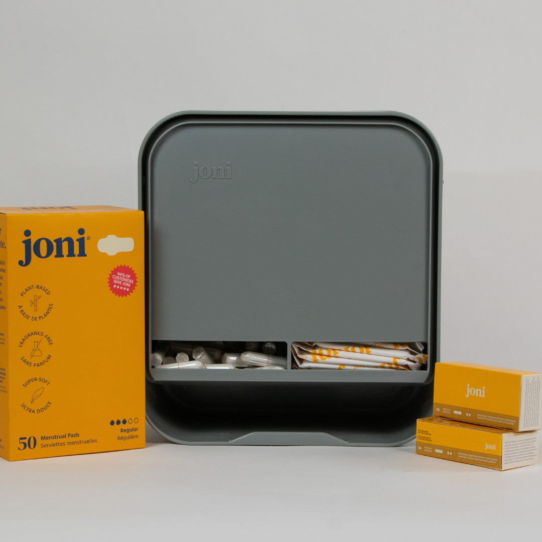 joni Model A open dispenser on grey background with pads and tampons