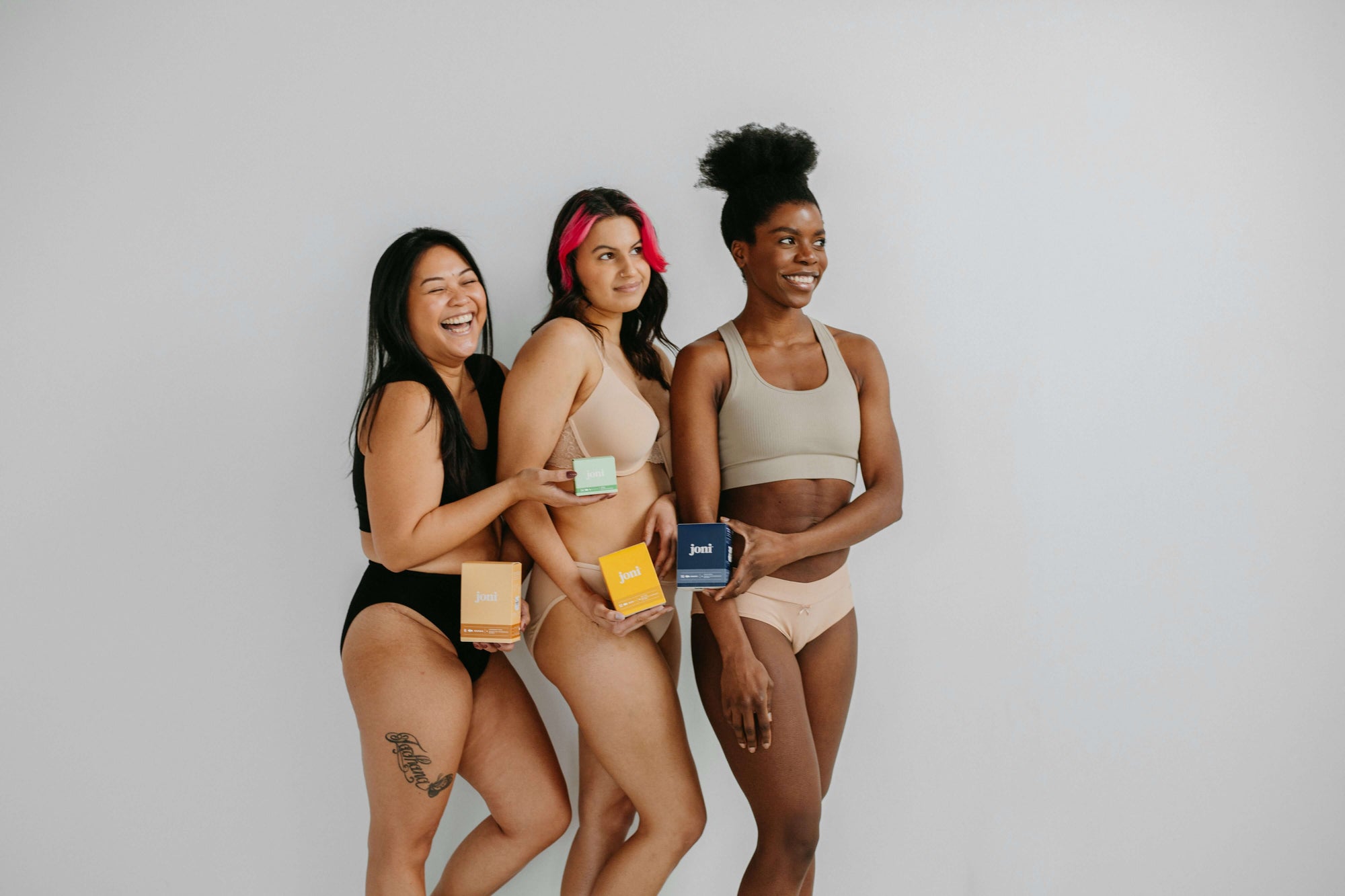Three women in underwear showcasing period care products, promoting support for period equity.