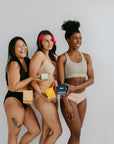 Three women in underwear showcasing period care products, promoting support for period equity.