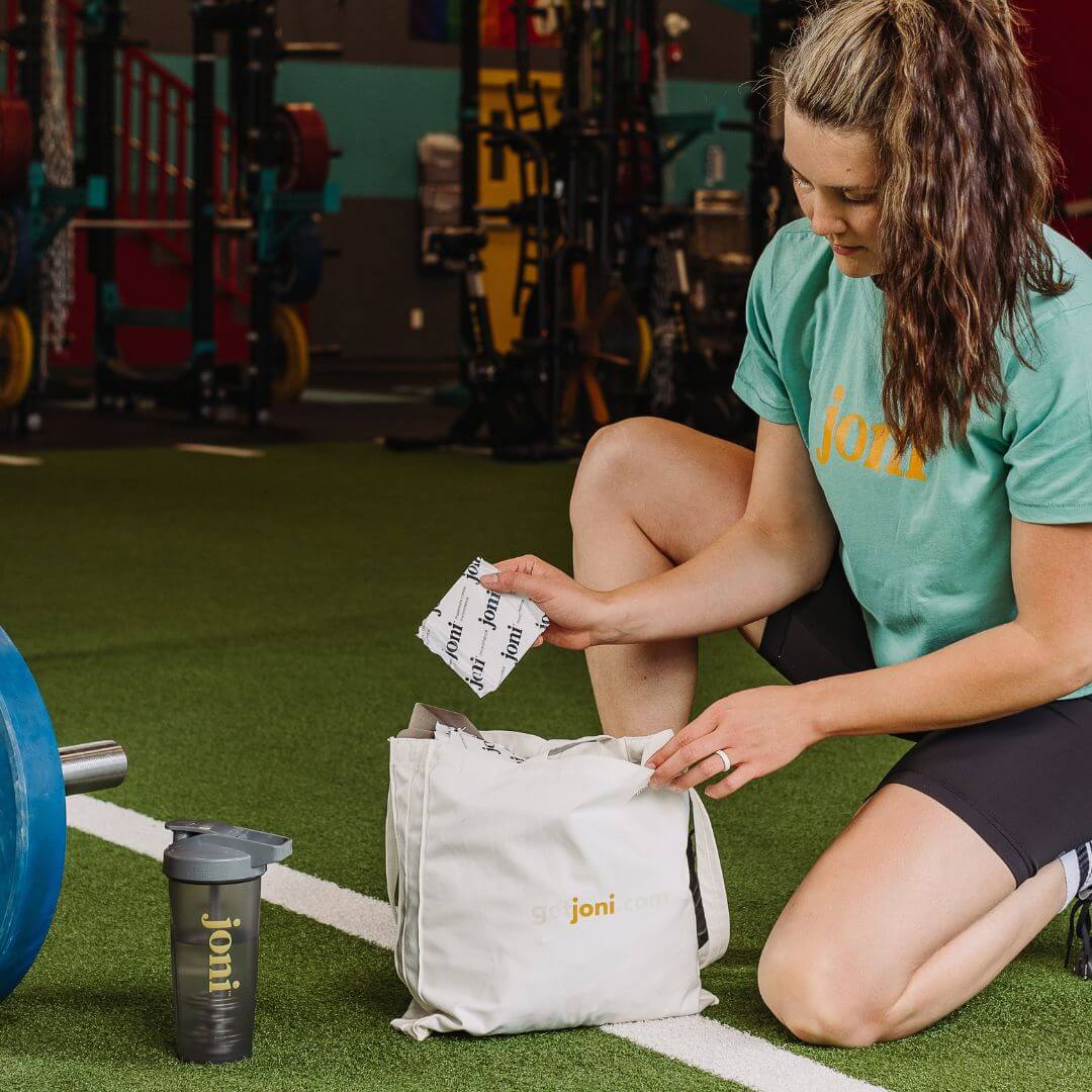 Woman at gym unpacking joni bamboo incontinence pads from tote bag for on-the-go protection.