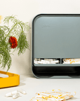 joni Model A period care dispenser on a washroom countertop with a plant