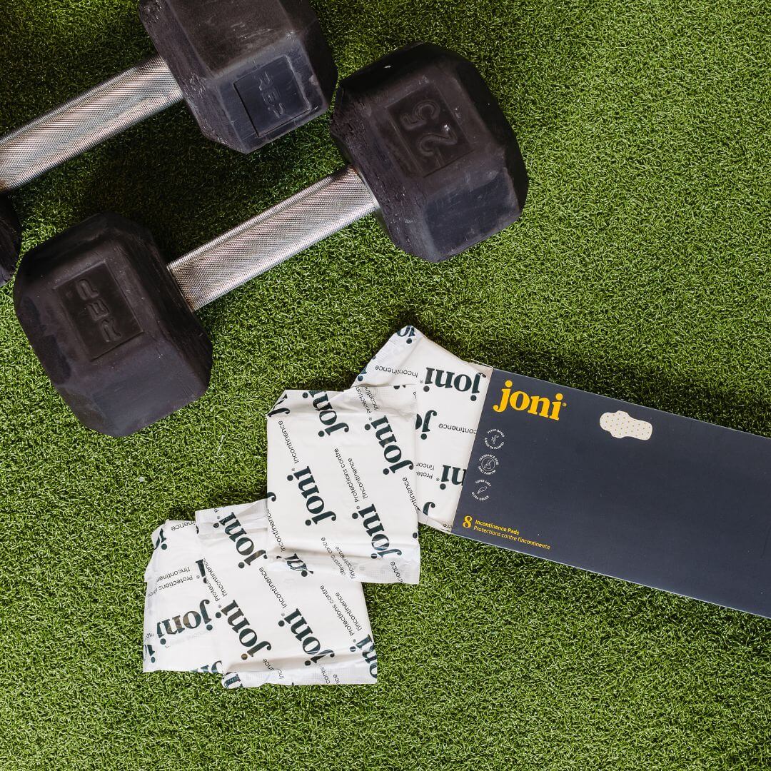 Bamboo incontinence pads by joni next to dumbbells on grass background, highlighting active lifestyle and leak protection.