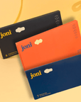 Postpartum Period Care Bundle featuring joni Organic Pads in black, orange, and blue packaging against a sunny backdrop.