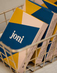 Colorful boxes of joni period care products arranged in a wire basket, promoting period equity.