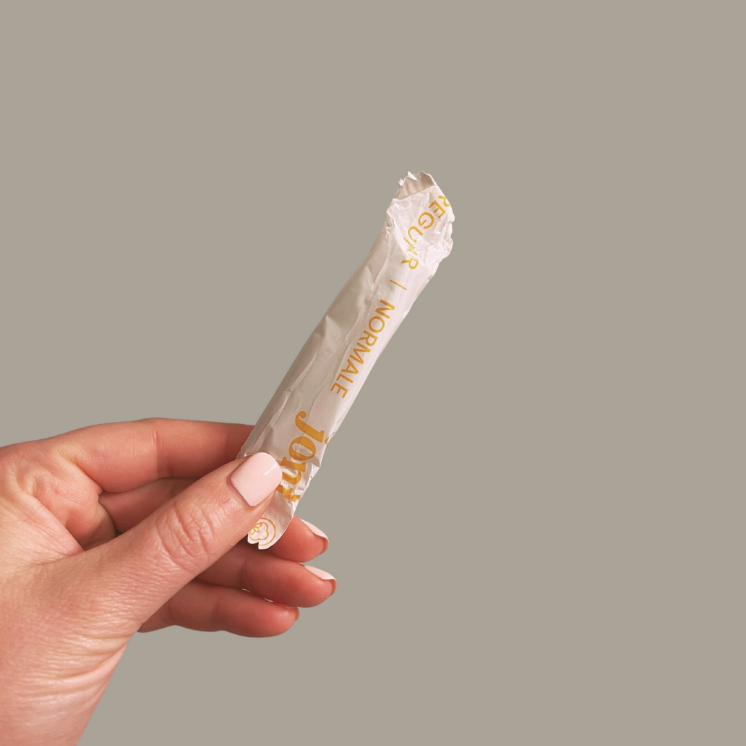 Hand holding a regular applicator tampon wrapped in recyclable packaging, showcasing organic cotton product.