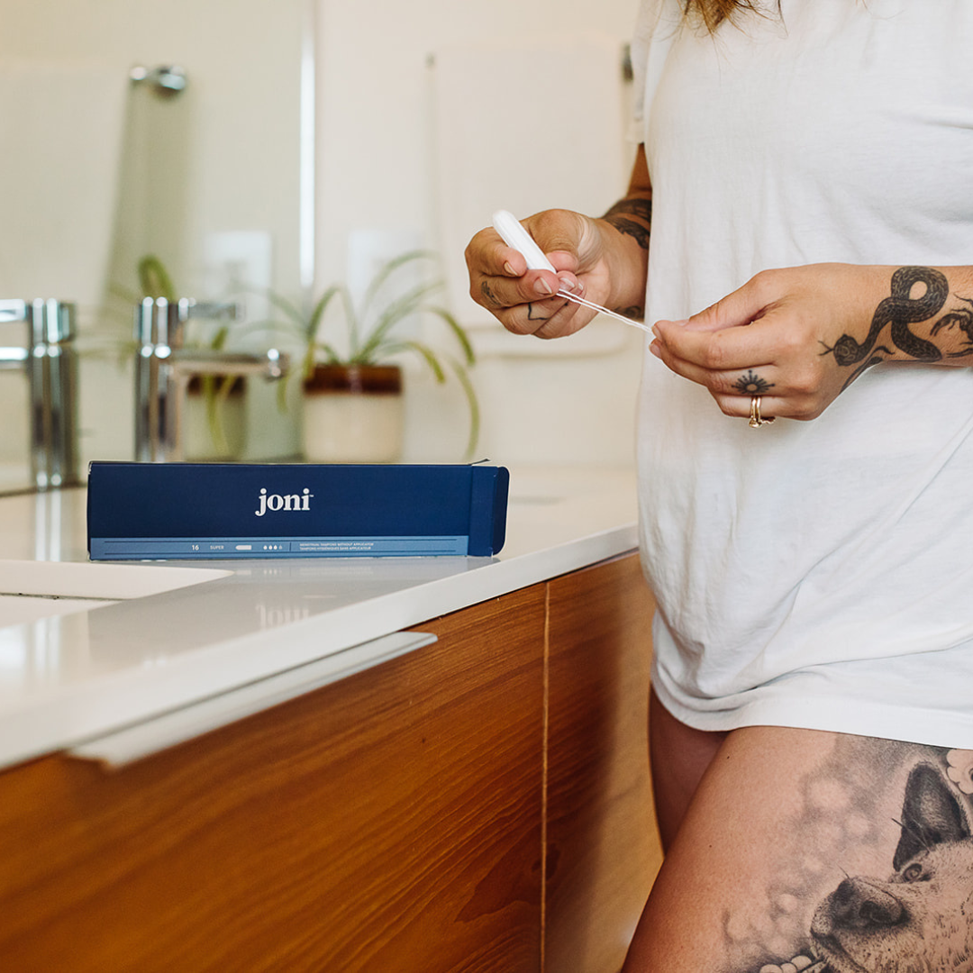 Person holding a joni organic cotton Super Non-Applicator Tampon next to a box in a bathroom setting.