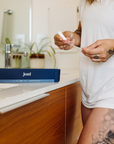 Person holding a joni organic cotton Super Non-Applicator Tampon next to a box in a bathroom setting.