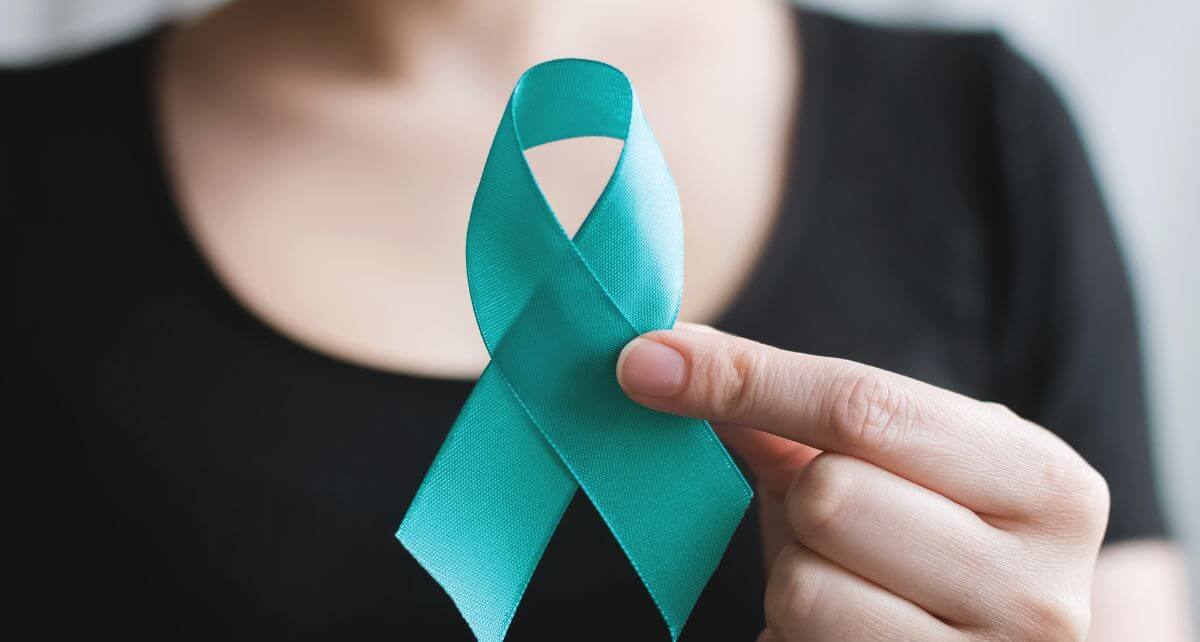 Person holding a teal ribbon symbolizing ovarian cancer awareness.
