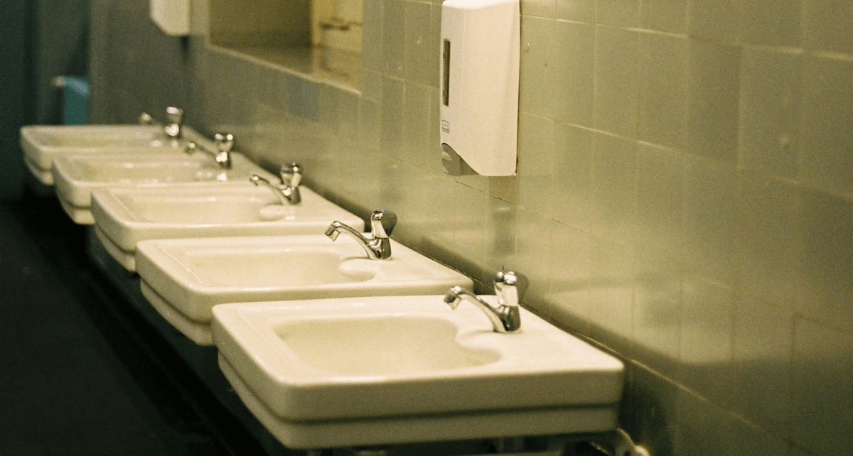 A row of white sinks in a school washroom. There is no period care receptacle in site.