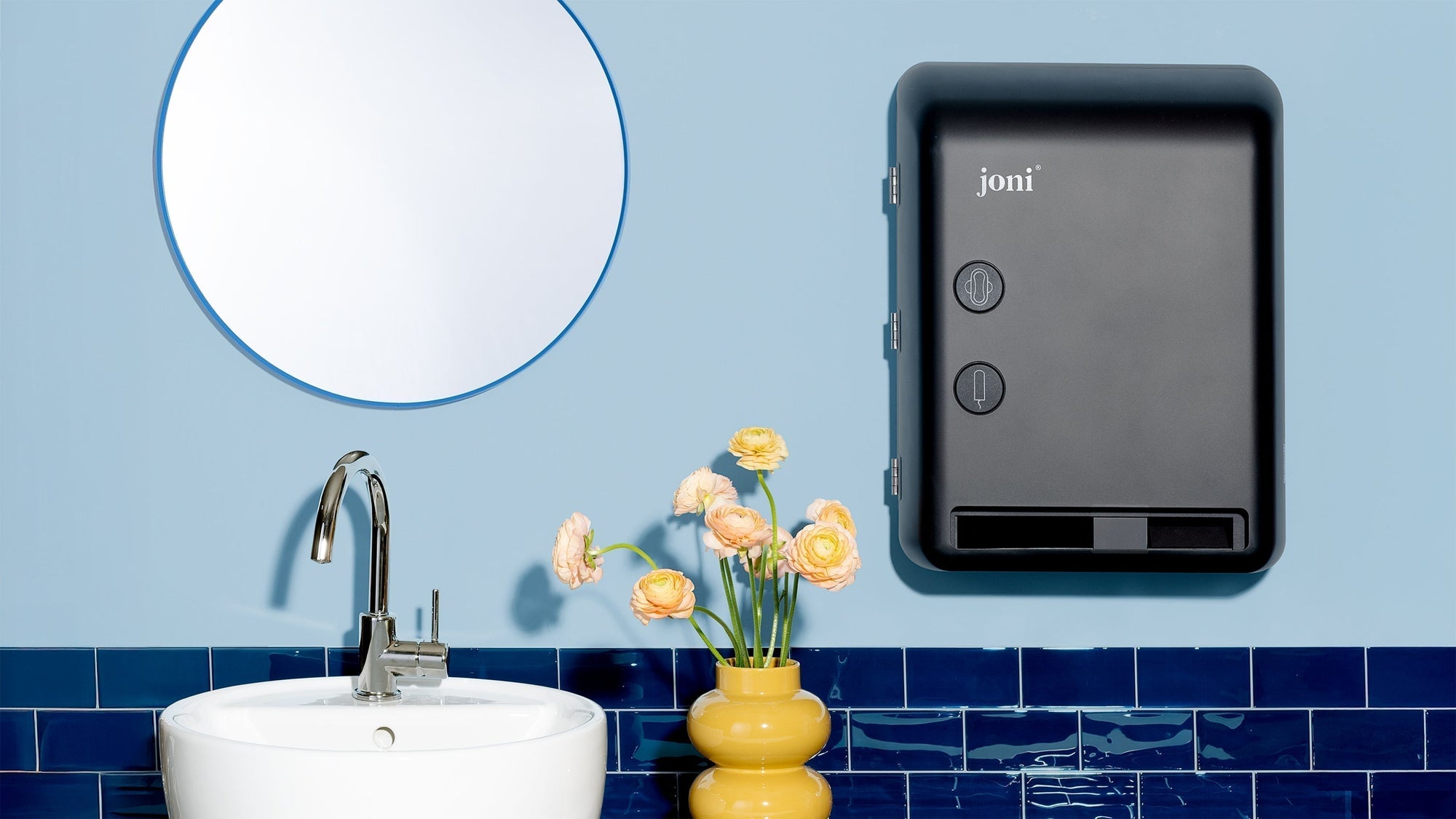 joni Model V smart dispenser hangs on blue wall in a modern washroom