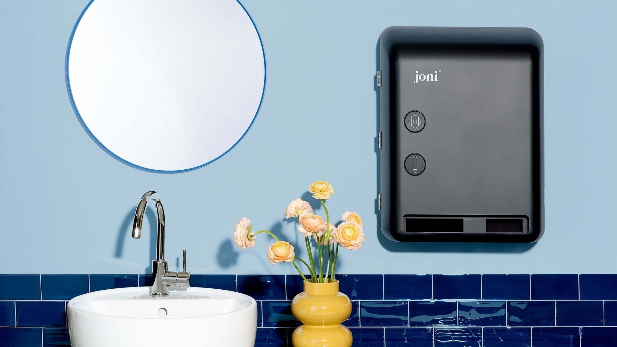 joni Model V smart dispenser hangs on blue wall in a modern washroom