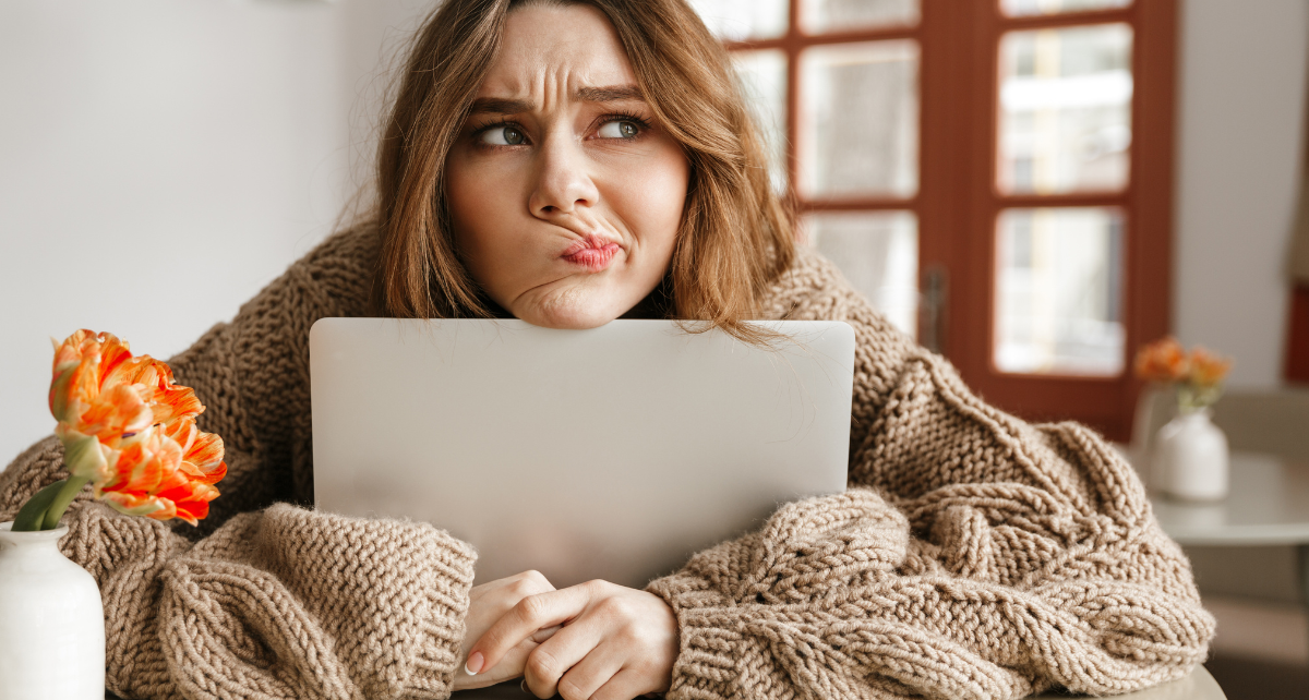 A woman rests her chin on her laptop looking confused as she contemplates her perimenopause symptoms