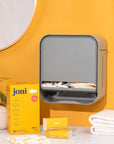 Modern joni open period care dispenser on a countertop with pads and tampons, set against a vibrant yellow wall.