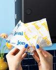 Hands holding multiple 'joni' brand packets with a blurred background