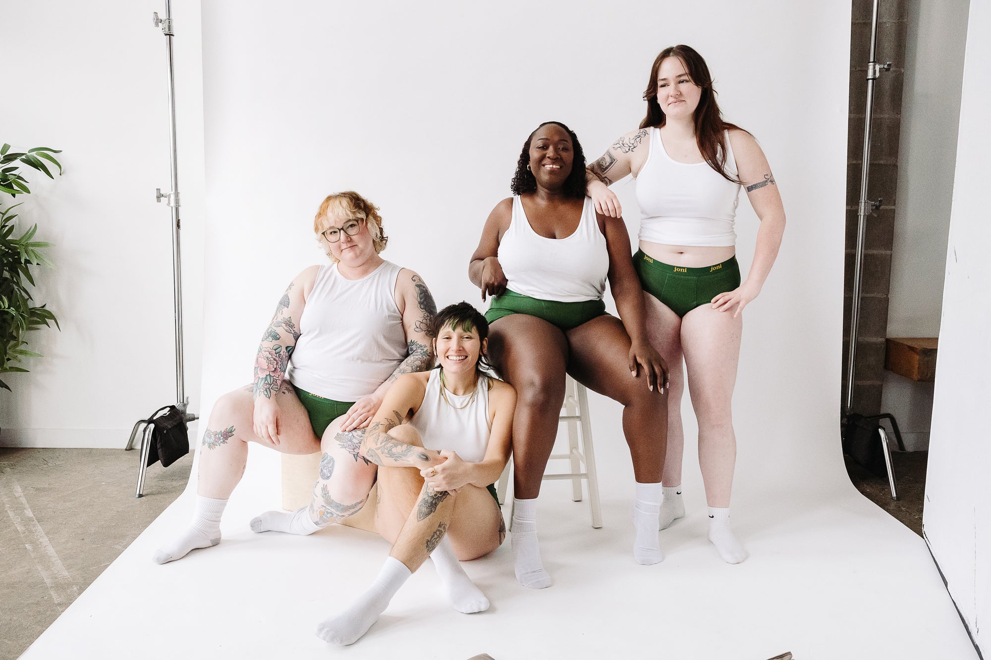 Four smiling menstruators of different sizes in joni period underwear wearing white tops against a white backdrop.
