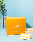 Yellow bulk box of joni regular pads with a blue background and a bamboo plant