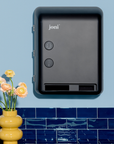 joni Model V electronic period care dispenser on a blue wall with blue tile and a yellow flower vase